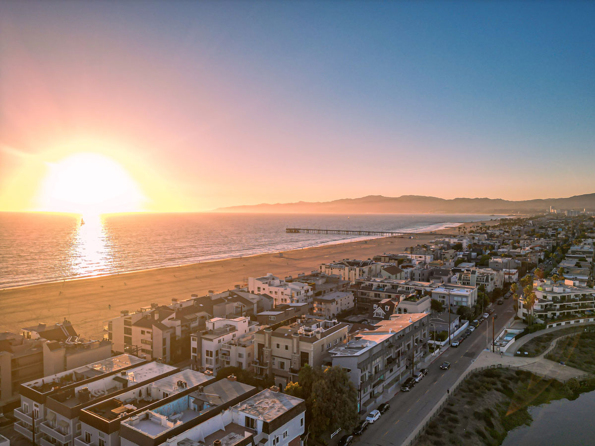Aerial view of Venice, California, featuring beachfront homes, the Pacific Ocean, Venice Beach, and the iconic Venice Fishing Pier at sunset.