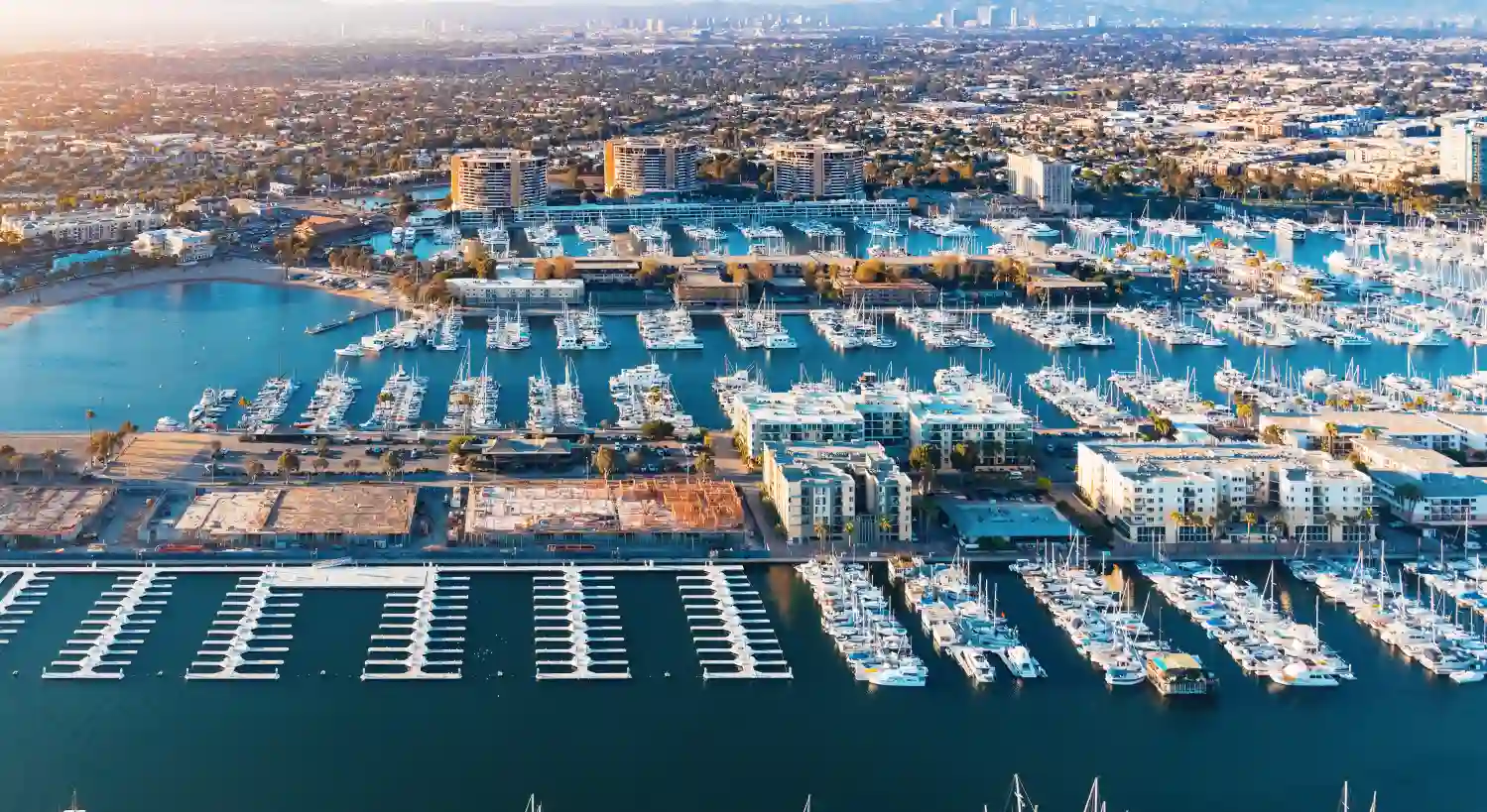 Panoramic aerial view of Marina del Rey featuring the marina, yacht harbor, waterfront residences, and Los Angeles skyline in the distance.