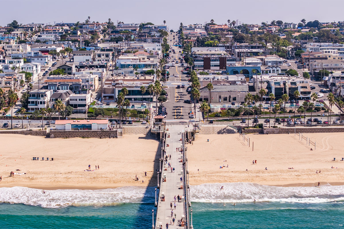 Wide aerial view of Manhattan Beach, California, featuring the Manhattan Beach Pier, Pacific Ocean, beachfront homes, and surrounding neighborhood.