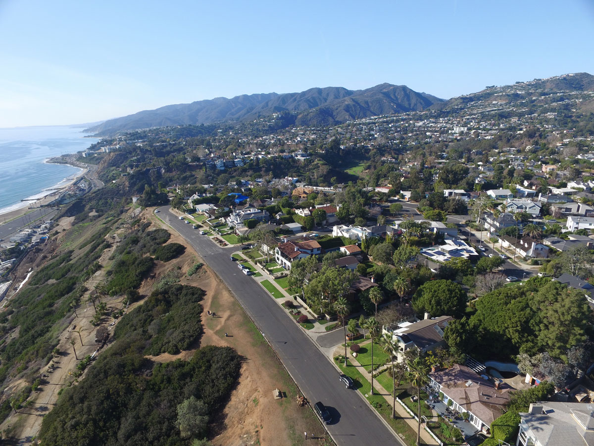 Wide aerial view of Pacific Palisades, California, showcasing coastal neighborhoods, scenic bluffs, the Pacific Ocean, and the Santa Monica Mountains.